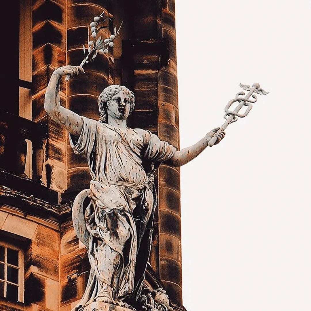 Stone statue of a classical goddess holding a caduceus and a bird, set against a grand ornate building facade