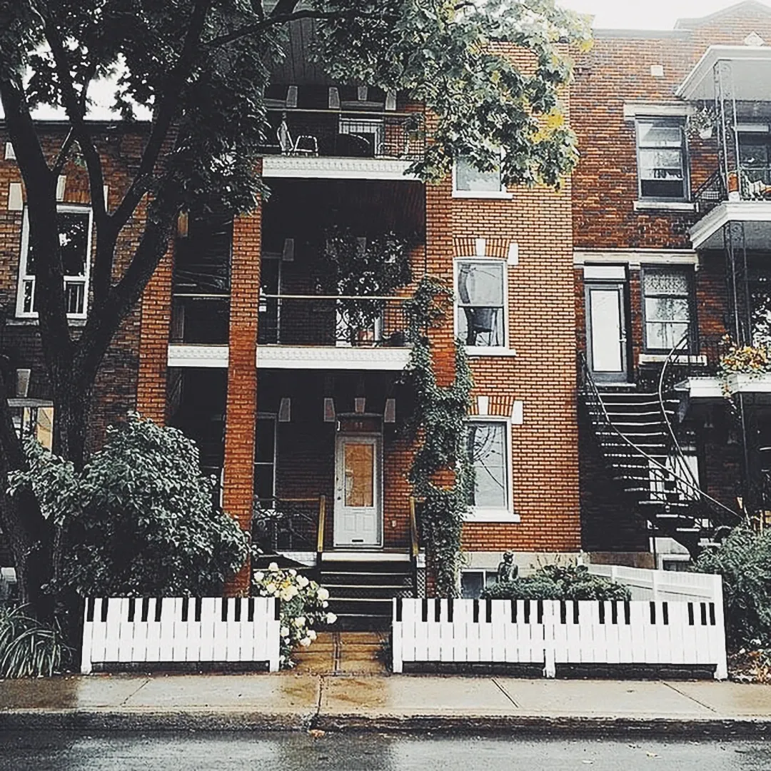 A Montreal brick duplex with a front fence painted as piano keys, spiral staircases and balconies draped in vines