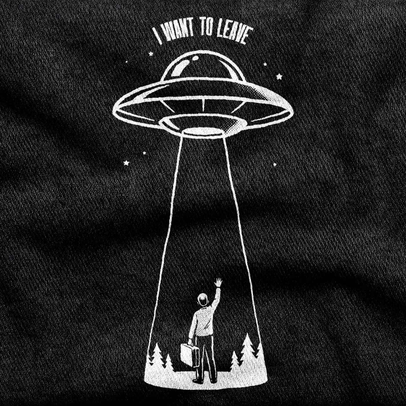 A lone figure with a packed suitcase reaching one arm up toward a flying saucer overhead, white on a black tee.