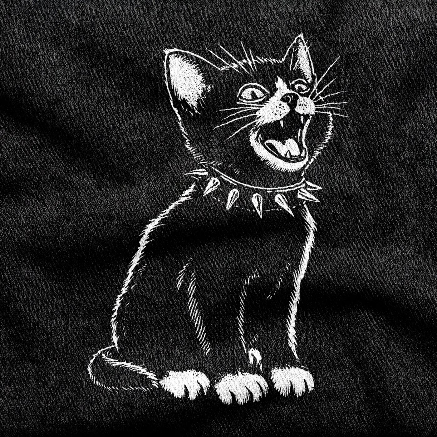 A small ferocious kitten in a studded torn collar with a nicked ear and a defiant stare, white on a black tee.