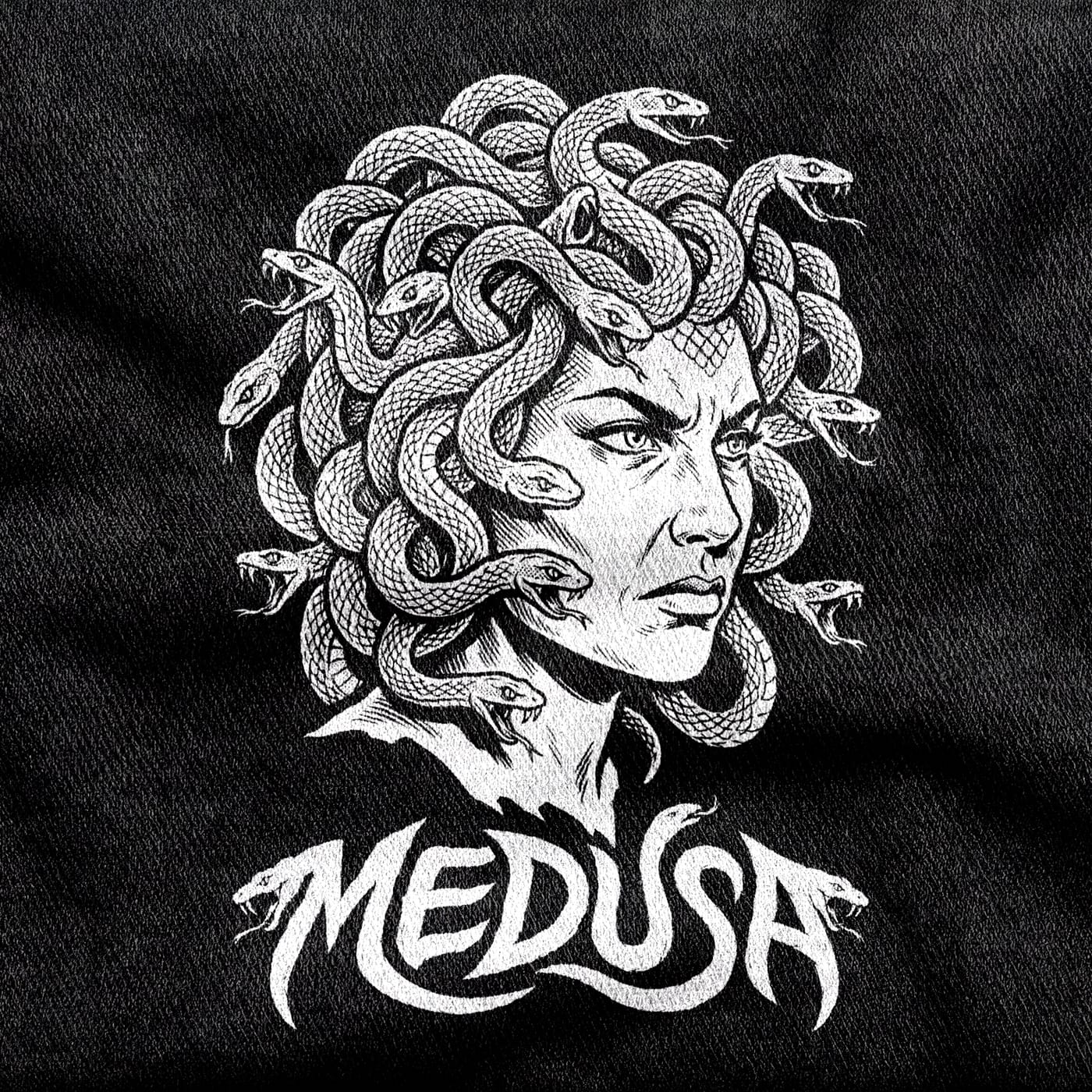 Medusa's grieving, angry face under a crown of coiling snakes, with a wordmark whose letters taper into snake heads, white on a black tee.
