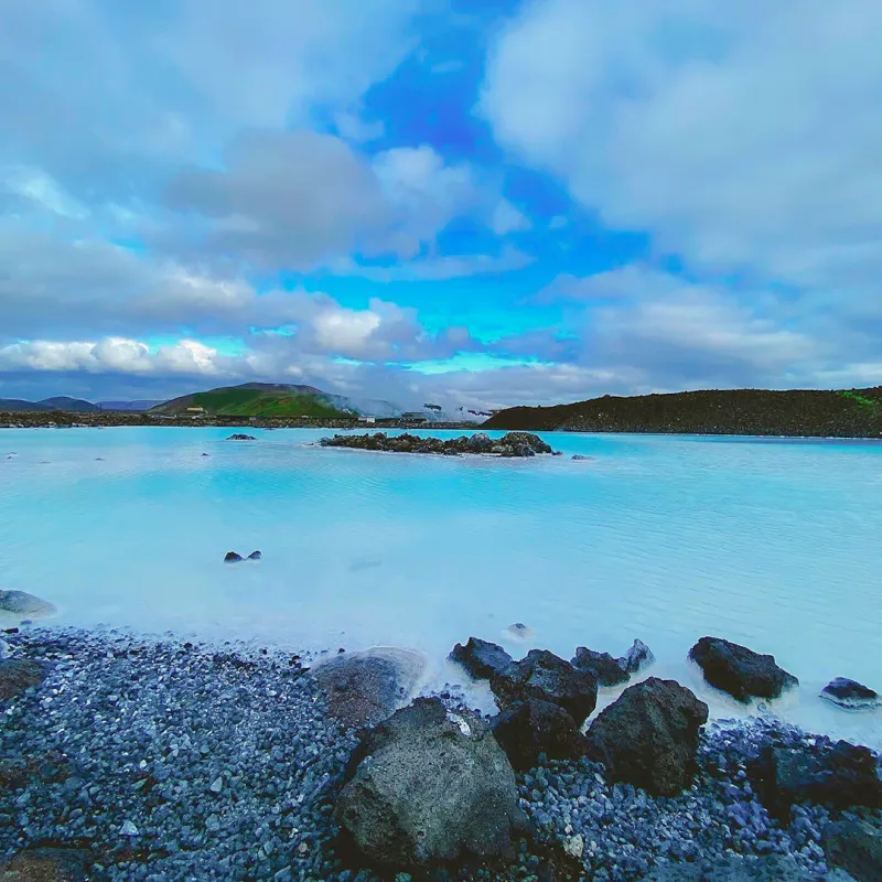Milky blue geothermal waters of Iceland's Blue Lagoon stretching toward green hills under a dramatic cloudy sky