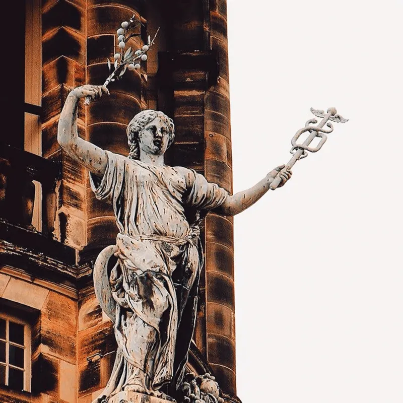 Stone statue of a classical goddess holding a caduceus and a bird, set against a grand ornate building facade