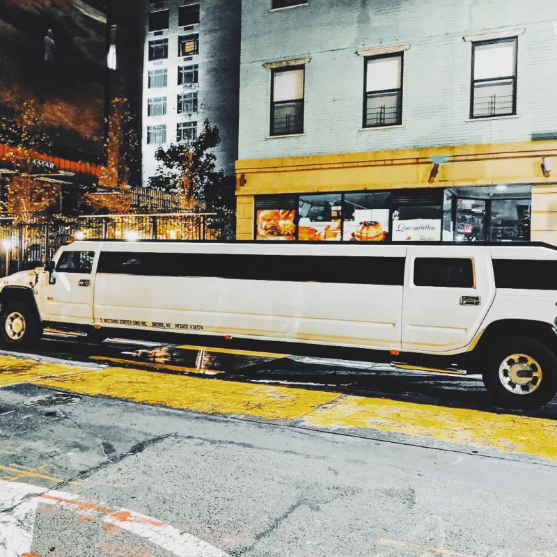 A white stretch Hummer limousine parked on a rain-slicked city street at night under yellow lights