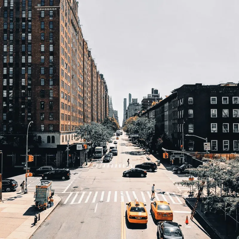 Looking down a wide New York City avenue lined with brick apartment buildings, yellow taxis at an intersection below