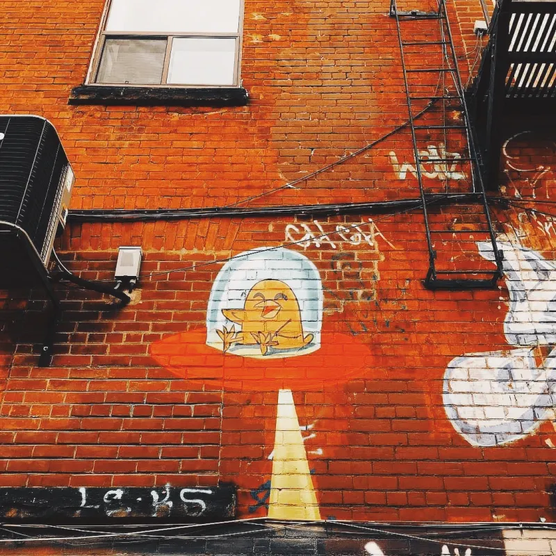 Street art of a golden bird trapped under a glass dome painted on a red brick wall in an alley with fire escapes