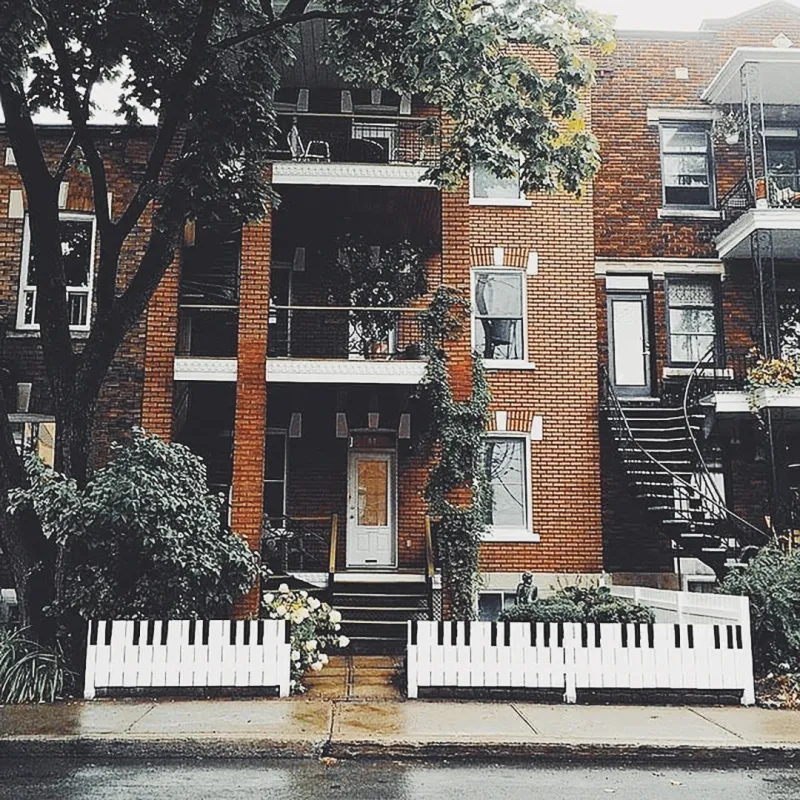 A Montreal brick duplex with a front fence painted as piano keys, spiral staircases and balconies draped in vines