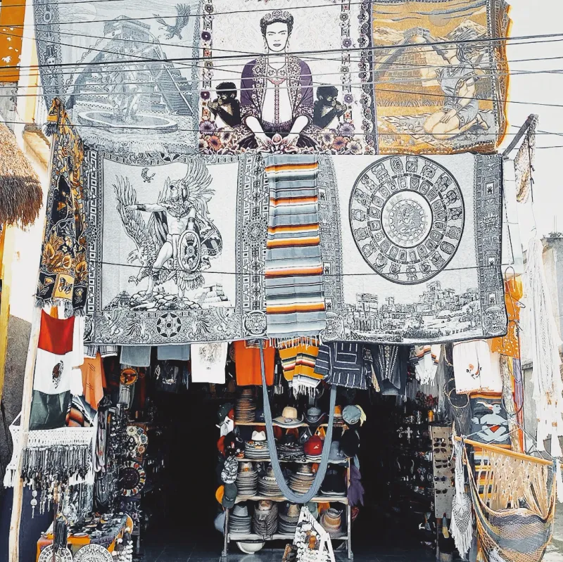 A Mexican market stall draped with colourful tapestries and textiles including a prominent Frida Kahlo portrait