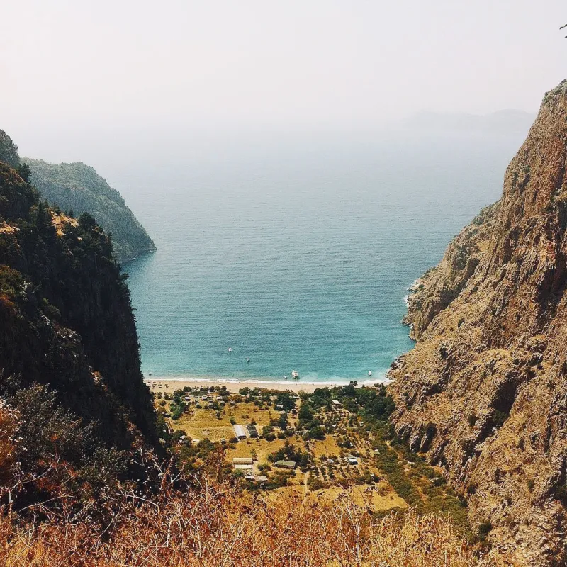 A narrow valley opening between rocky cliffs to reveal a turquoise bay and small village far below