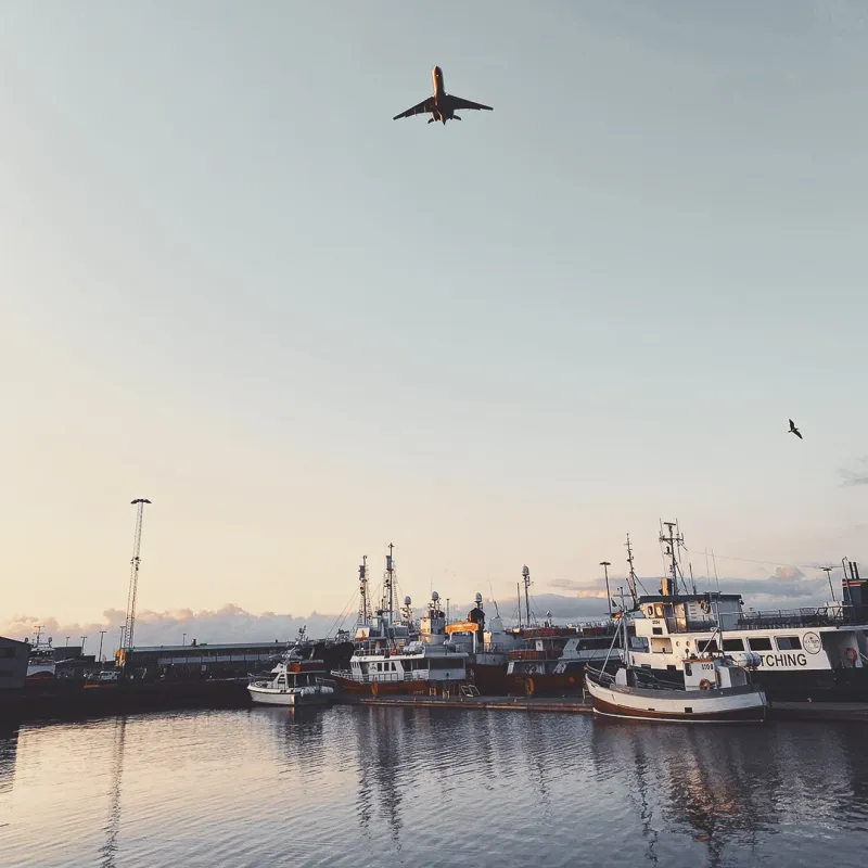 A commercial airplane ascending over a harbour of fishing vessels at golden hour in Reykjavik