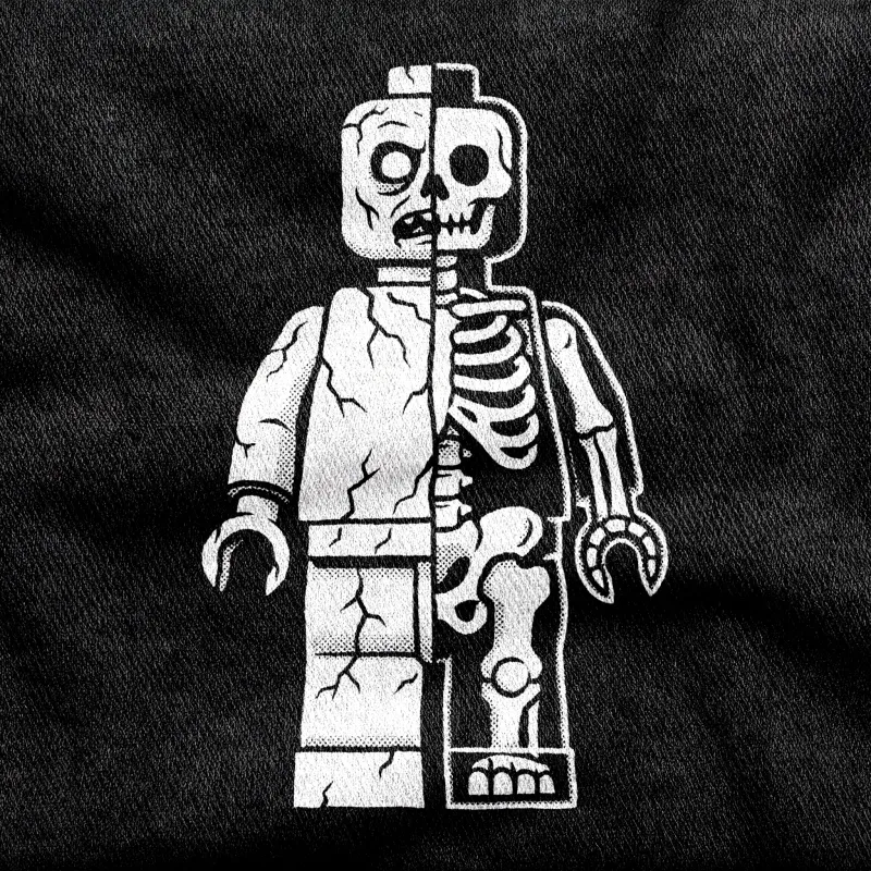 A toy minifigure split down the middle to show flesh on one side and skeleton on the other, grinning, white on a black tee.
