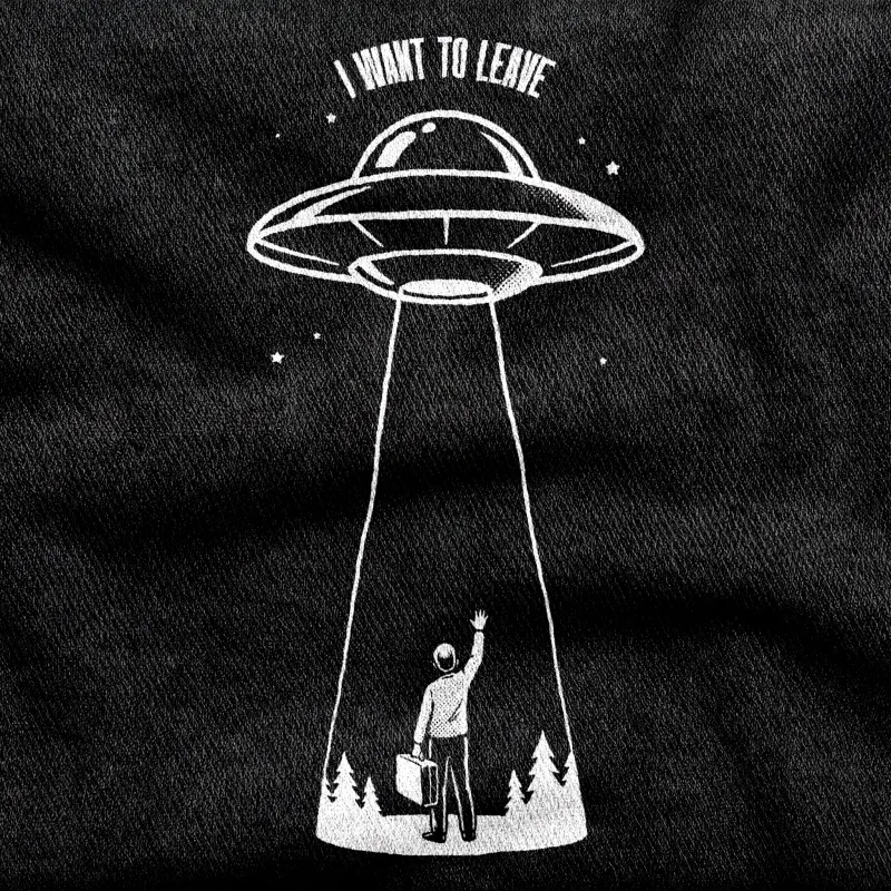 A lone figure with a packed suitcase reaching one arm up toward a flying saucer overhead, white on a black tee.