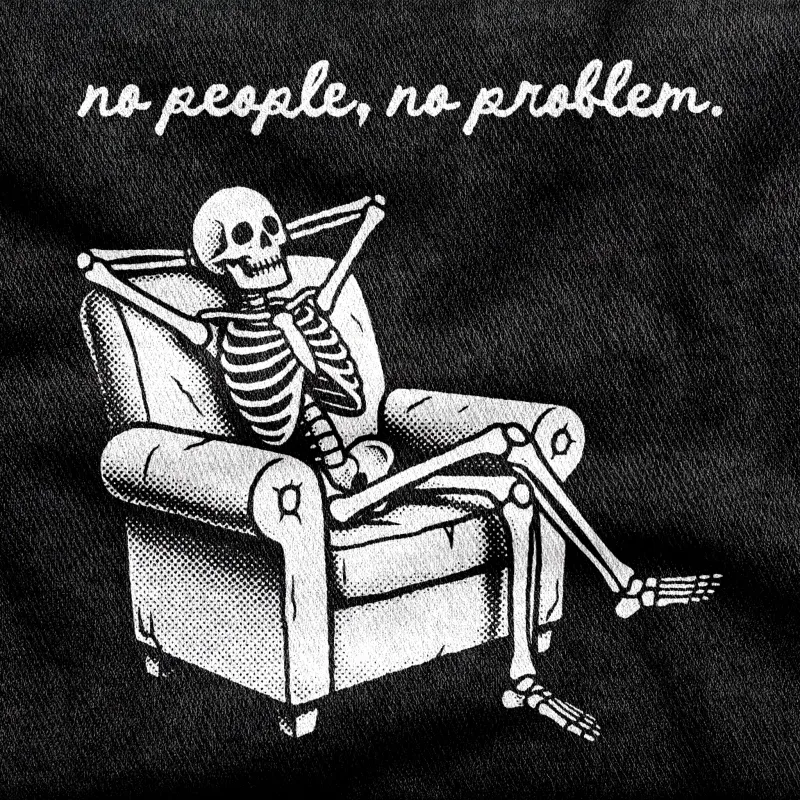 A skeleton lounging at ease in a battered armchair, ankles crossed and hands behind its skull, white on a black tee.