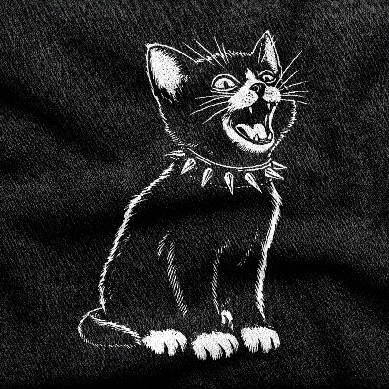 A small ferocious kitten in a studded torn collar with a nicked ear and a defiant stare, white on a black tee.