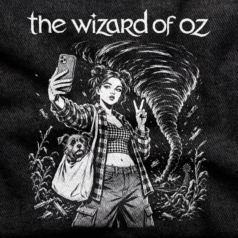 Dorothy in space buns and an open flannel over gingham, taking a selfie with Toto in a tote bag while a tornado tears up the farm behind her, white on a black tee.