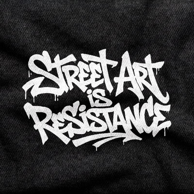 Marker handstyle with running drips reading "Street Art is Resistance", white on a black tee.