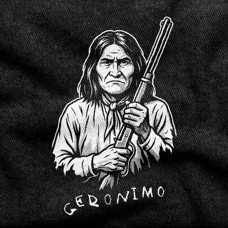 The Chiricahua Apache leader Geronimo holding a lever-action rifle upright, neckerchief at his throat, above his handwritten signature, white on a black tee.