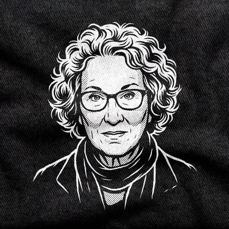 A portrait of the novelist Margaret Atwood under her halo of curls, glasses on, looking straight out, white on a black tee.