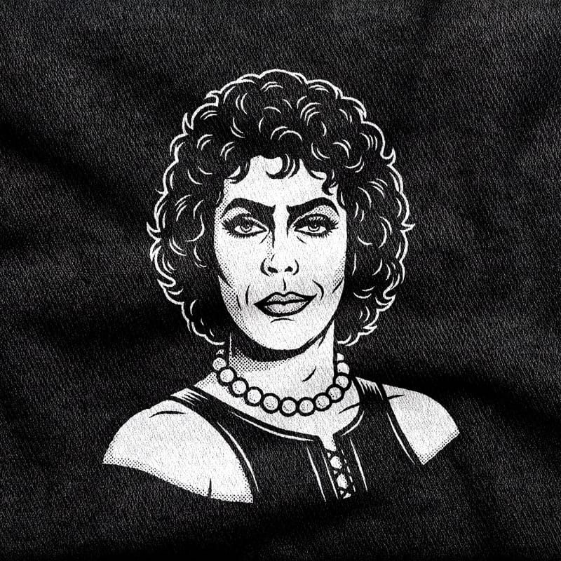 Frank-N-Furter in pearls and a boned corset, shoulders bare and eyes heavily made up, looking directly out, white on a black tee.