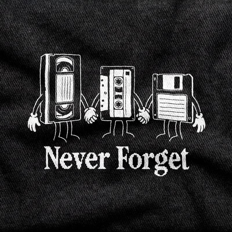 A VHS tape, a cassette and a floppy disk with rubber-hose arms and white gloves, standing in a row holding hands above the words "Never Forget", white on a black tee.